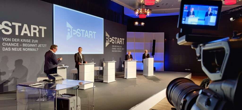 Die Gäste und Moderatoren sind auf der Bühne und die Kamera filmt das hybride Event